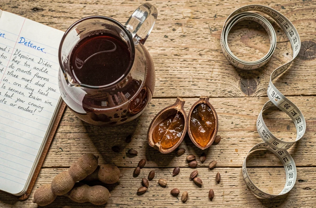 Gros plan sur du jus de tamarin frais, des gousses de tamarin et un journal de régime détox posés sur une table en bois